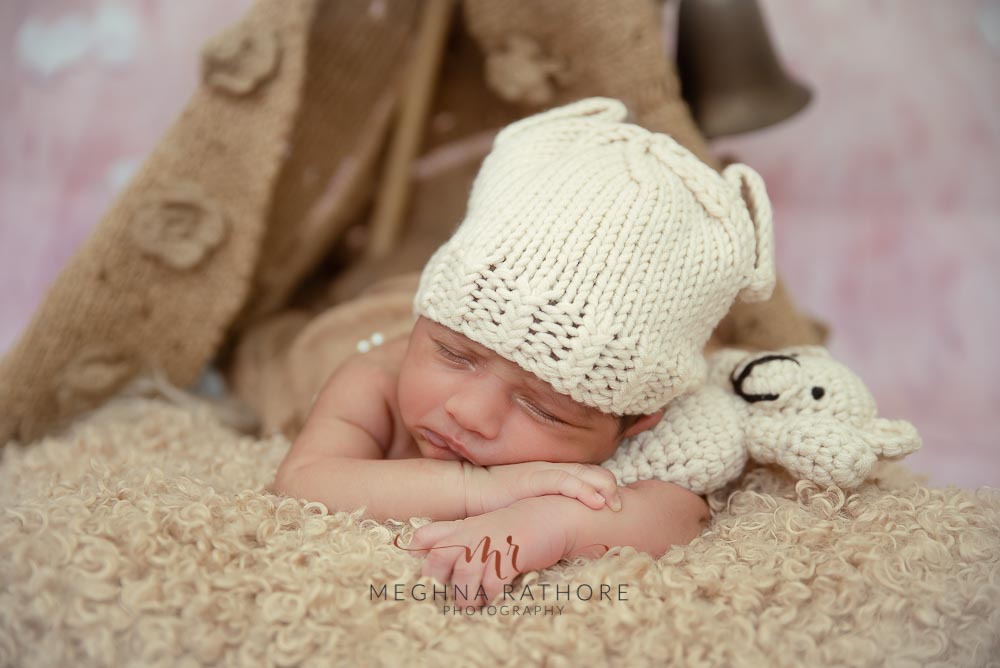 23 days old newborn baby boy with a white woolen cap and a toy beside with other props at meghna rathore photography in delhi