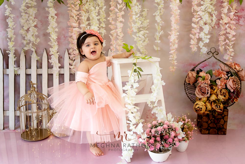 1 year old girl posing standing against a ladder for professional photoshoot at meghna rathore photography in delhi gurgaon