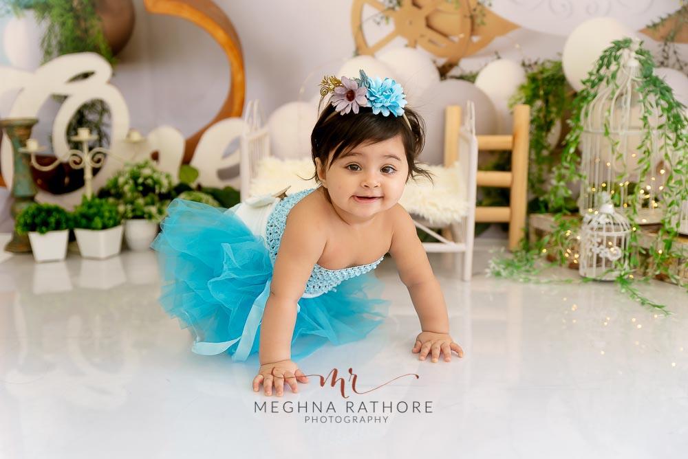 1 year old girl posing in a blue colored frock and crawling for professional photoshoot at meghna rathore photography in delhi gurgaon