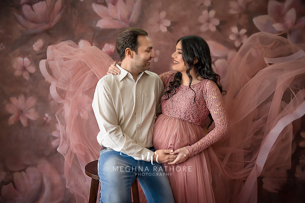 Professional shoot of Mother-to-be with partner in peach gown and white shirt during maternity shoot with floral background in Delhi