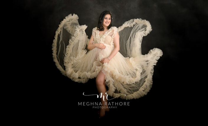 Delhi best maternity photographer, best photoshoot picture in indoor studio with mother in off white dress and holding tummy