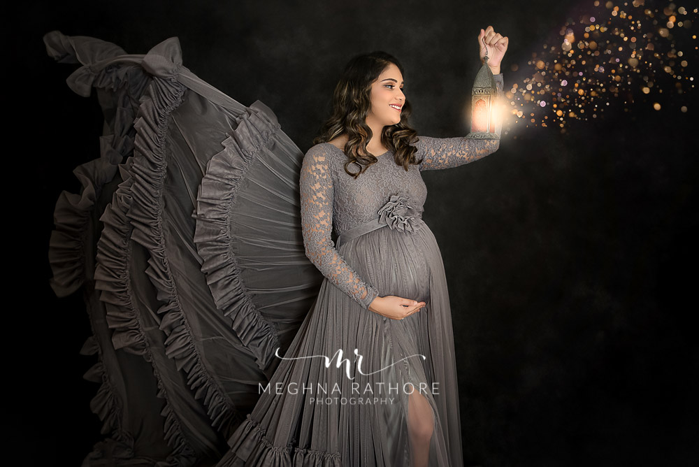 expecting mother pregnancy photo shoot holding lantern with magical pixie dust coming black backdrop