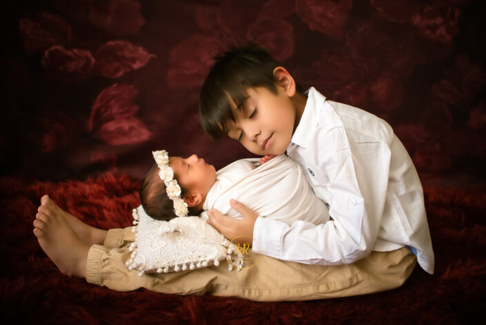A boy and his babysister resting together on a red blanket captured by Delhi NCR's best maternal photographer Meghna Rathore.