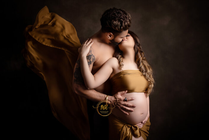 Expectant couple in matching golden attire, holding hands and smiling, anticipating the arrival of their baby captured by Delhi NCR's best maternal photographer Meghna Rathore.