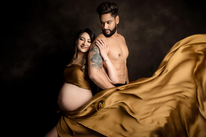 An expectant couple happily posing for a picture in coordinating golden attire captured by Delhi NCR's best maternal photographer Meghna Rathore.