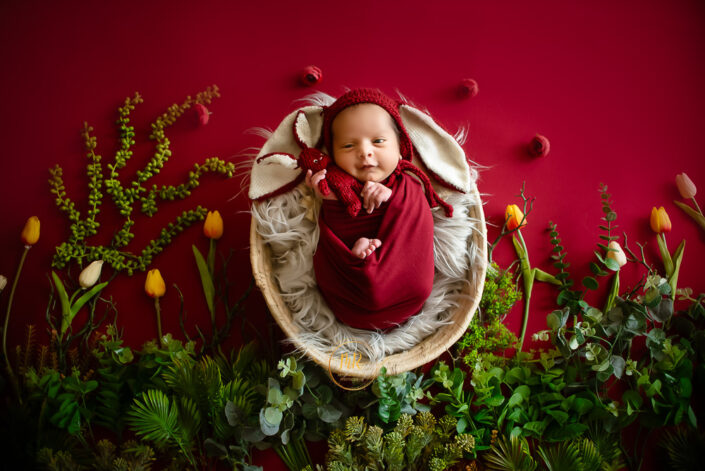 A baby in a red wrap laying on a red background captured by Delhi NCR's best maternal photographer Meghna Rathore.