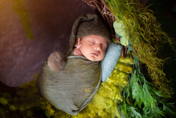 Newborn baby boy napping in a green basket captured by Delhi NCR's best maternal photographer Meghna Rathore.