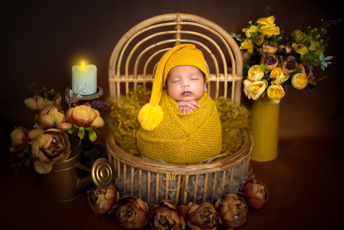 Newborn baby boy wrapped in a yelloww blanket inside a bucket surrounded by candles and flowers captured by Delhi NCR's best maternal photographer Meghna Rathore.