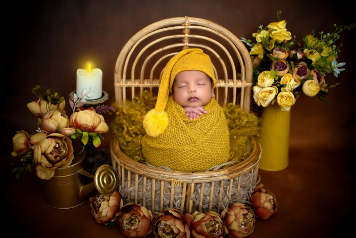Newborn baby boy wrapped in a yelloww blanket inside a bucket surrounded by candles and flowers captured by Delhi NCR's best maternal photographer Meghna Rathore.