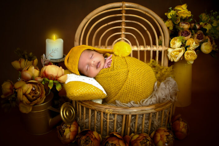 Newborn baby boy wrapped in a yelloww blanket inside a bucket surrounded by candles captured by Delhi NCR's best maternal photographer Meghna Rathore.