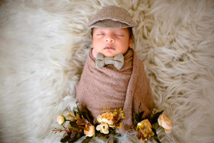 A newborn baby boy in a brown hat and bow tie captured by Delhi NCR's best maternal photographer Meghna Rathore.