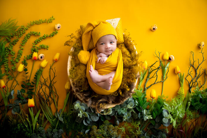 A baby in a yellow wrap on a yellow floral background captured by Delhi NCR's best maternal photographer Meghna Rathore.