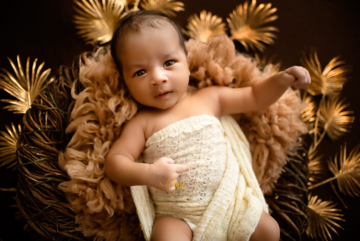 Infant in white dress on brown flowery background captured by Delhi NCR's best maternal photographer Meghna Rathore.