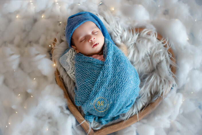 A newborn baby boy peacefully sleeping on a blue blanket, surrounded by white fluffy clouds captured by Delhi NCR's best maternal photographer Meghna Rathore.