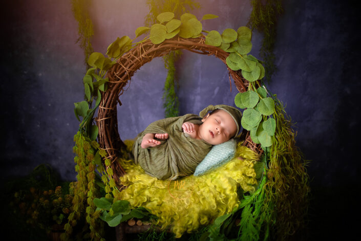 A newborn baby boy wrapped in a green blanket sitting in a wooden basket captured by Delhi NCR's best maternal photographer Meghna Rathore.