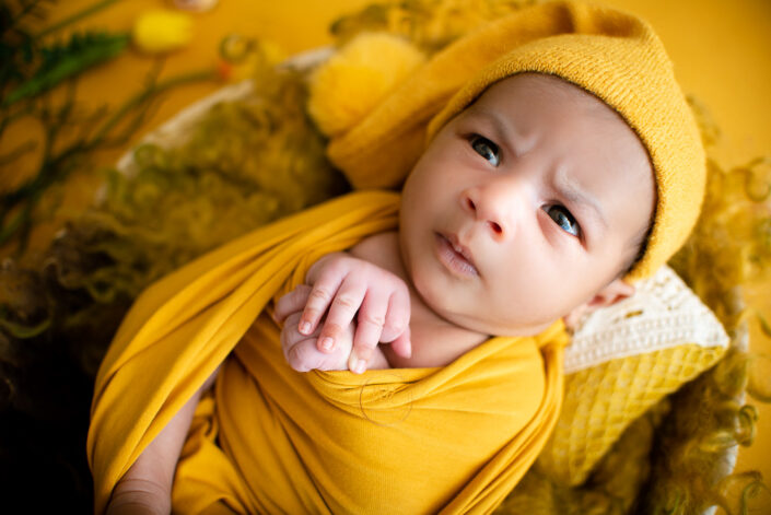 A baby in a yellow wrap on a yellow floral background captured by Delhi NCR's best maternal photographer Meghna Rathore.