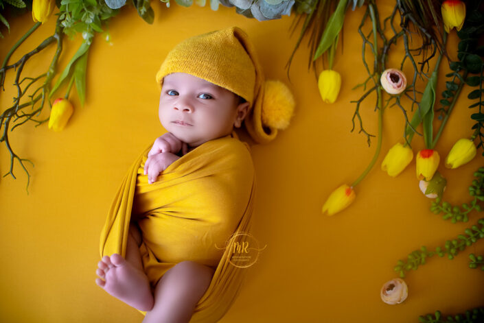A baby in a yellow wrap on a yellow floral background captured by Delhi NCR's best maternal photographer Meghna Rathore.