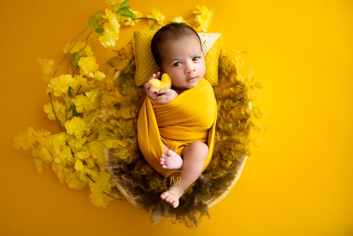 A baby in a yellow wrap on a yellow floral background captured by Delhi NCR's best maternal photographer Meghna Rathore.