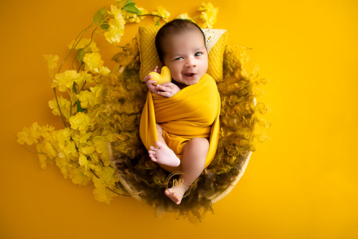 A baby in a yellow wrap on a yellow floral background captured by Delhi NCR's best maternal photographer Meghna Rathore.