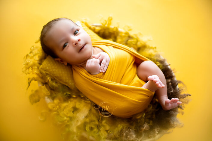 A baby in a yellow wrap on a yellow background captured by Delhi NCR's best maternal photographer Meghna Rathore.