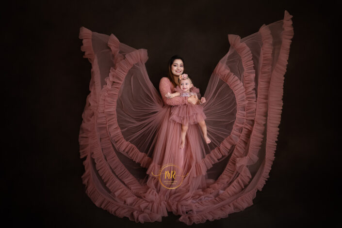 A woman in a pink dress cradling a baby in her arms, radiating love and tenderness captured by Delhi NCR's best maternal photographer Meghna Rathore.