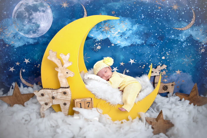 A newborn baby girl peacefully sleeping on a crescent moon in a serene photo captured by Delhi NCR's best maternal photographer Meghna Rathore.