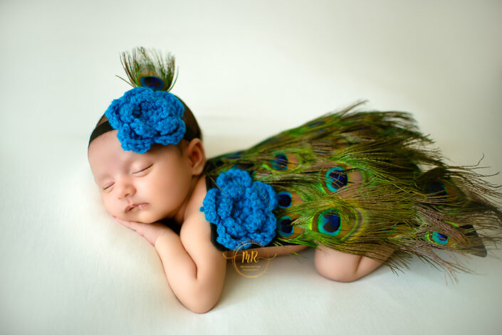 A baby girl in a blue peacock costume, looking adorable and colorful captured by Delhi NCR's best maternal photographer Meghna Rathore.