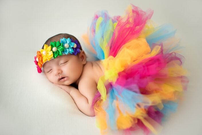 A newborn girl in a vibrant tutu and headband, looking adorable captured by Delhi NCR's best maternal photographer Meghna Rathore.