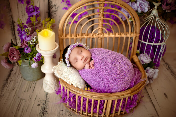 A newborn girl peacefully sleeping in a wicker basket surrounded by purple flower captured by Delhi NCR's best maternal photographer Meghna Rathore.