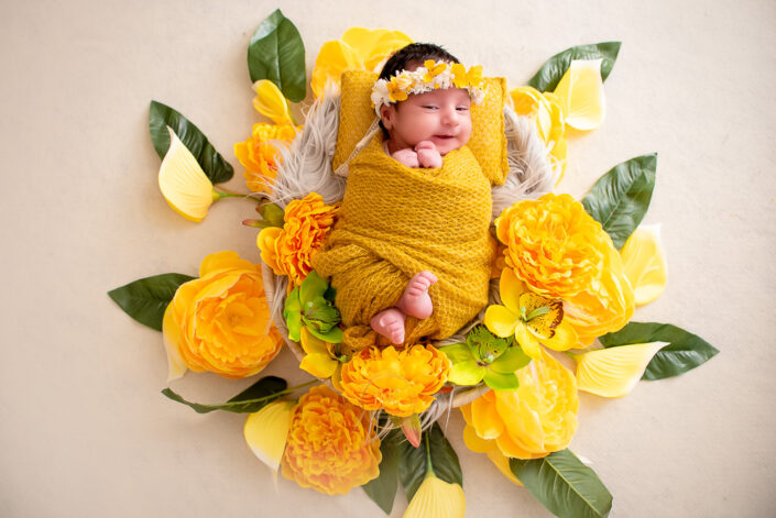 A newborn girl in yellow blanket surrounded by yellow flowers captured by Delhi NCR's best maternal photographer Meghna Rathore.