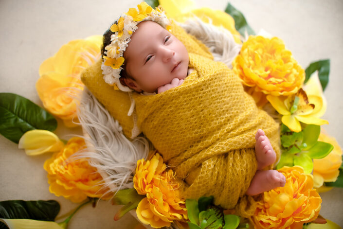 A newborn girl in yellow blanket surrounded by yellow flowers captured by Delhi NCR's best maternal photographer Meghna Rathore.