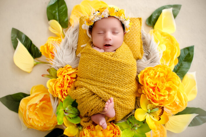 A newborn girl in yellow blanket surrounded by yellow flowers captured by Delhi NCR's best maternal photographer Meghna Rathore.
