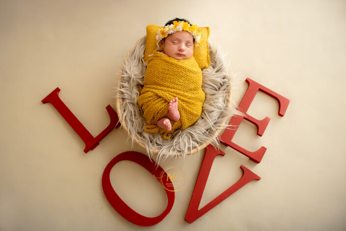 A newborn wrapped in a yellow blanket surrounded by the letters of the word "Love" captured by Delhi NCR's best maternal photographer Meghna Rathore.