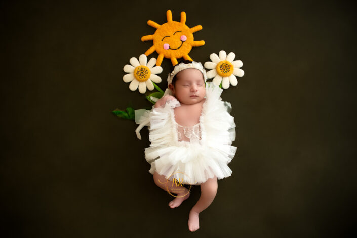 A newborn girl in a white dress with a sunflower headband captured by Delhi NCR's best maternal photographer Meghna Rathore.