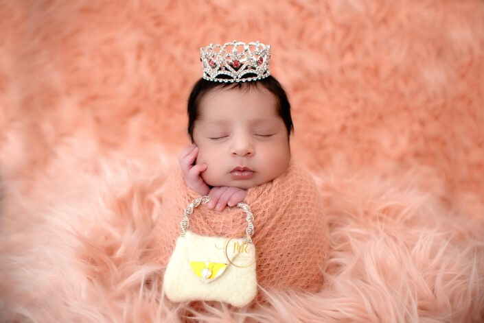 Newborn baby girl wrapped in pink with a shopping bag ,wearing a silver crown captured by Delhi NCR's best maternal photographer Meghna Rathore.