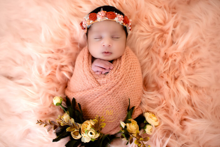 Newborn baby girl wrapped in pink with floral accents captured by Delhi NCR's best maternal photographer Meghna Rathore.