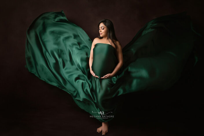 A pregnant woman in a green dress smiling for a photo captured by Delhi NCR's best maternal photographer Meghna Rathore.