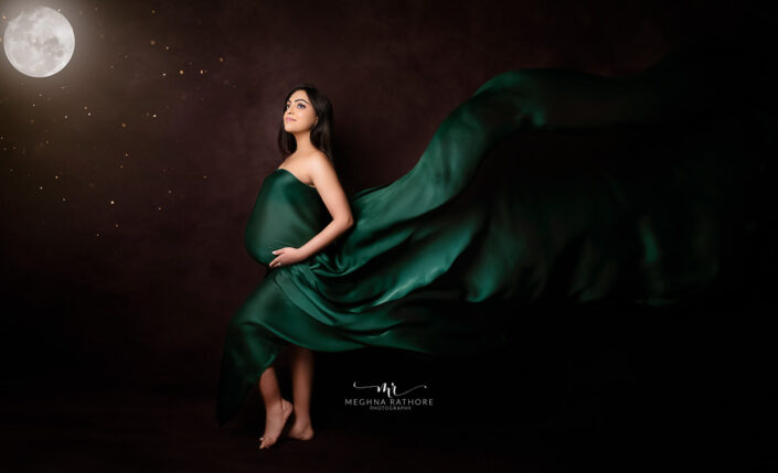 A pregnant woman in a green dress standing in front of the moon captured by Delhi NCR's best maternal photographer Meghna Rathore.