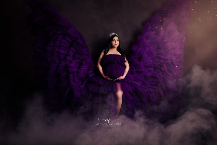 A pregnant woman in a purple dress with wings, symbolizing grace and beauty during maternity captured by Delhi NCR's best maternal photographer Meghna Rathore.
