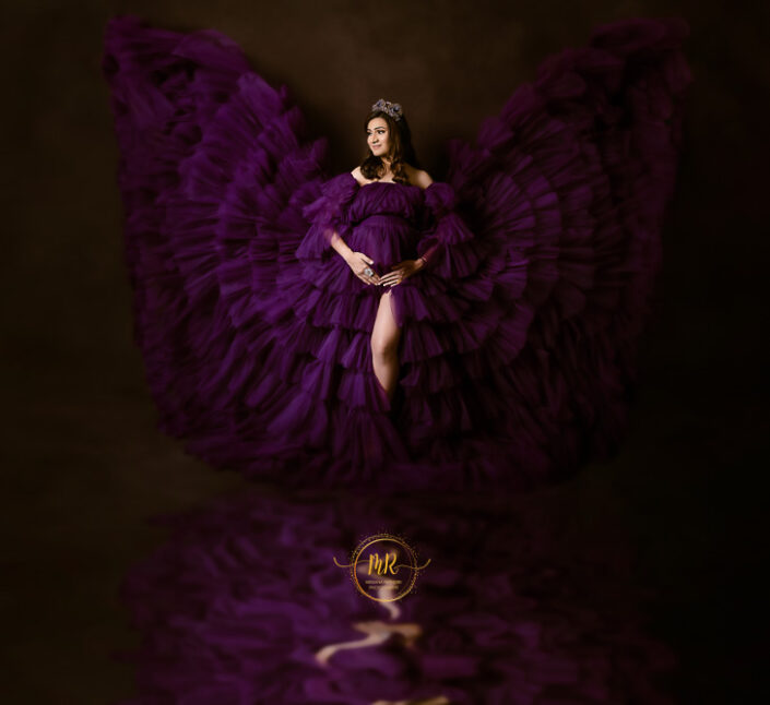 A pregnant woman in a purple dress with wings, standing gracefully captured by Delhi NCR's best maternal photographer Meghna Rathore.
