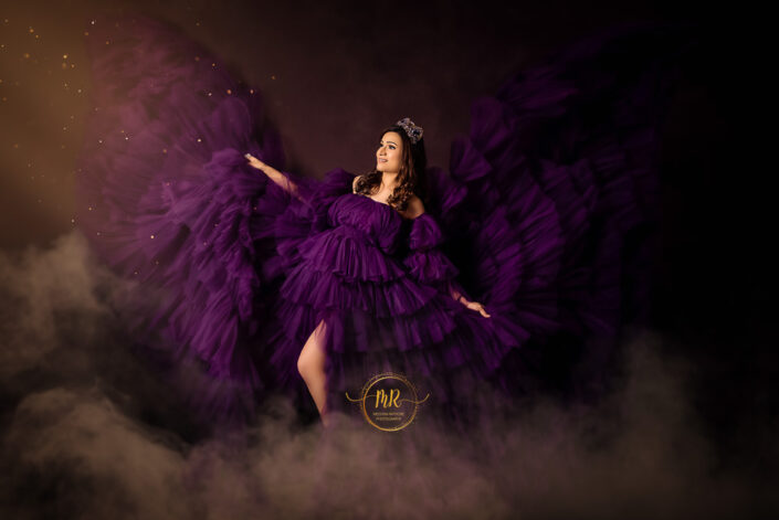 A pregnant woman in a purple dress with wings, standing gracefully captured by Delhi NCR's best maternal photographer Meghna Rathore.