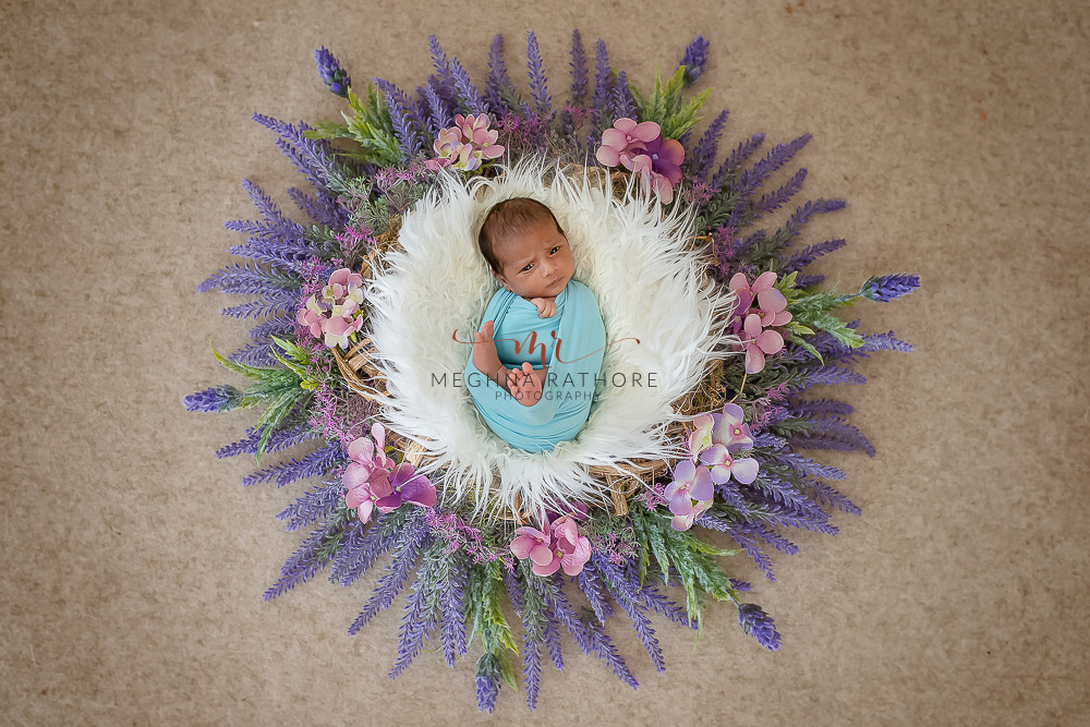 newborn baby boy tucked in a basket surrounded with flowers and leaves and posing at meghna rathore photography in delhi