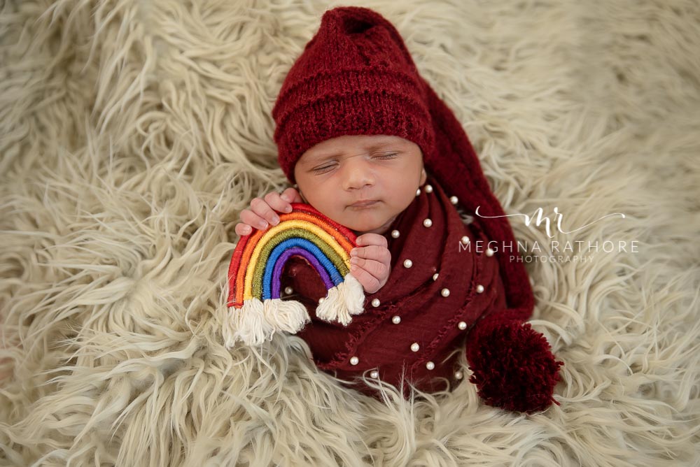 23 days old baby boy holding a rainbow woven toy in hand and posing at meghna rathore photography at delhi