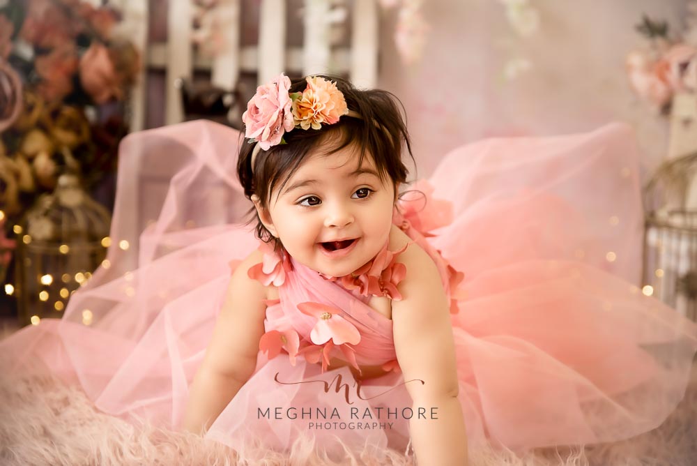 1 year old girl posing in a pink frock and smiling candidly for professional photoshoot at meghna rathore photography in delhi gurgaon