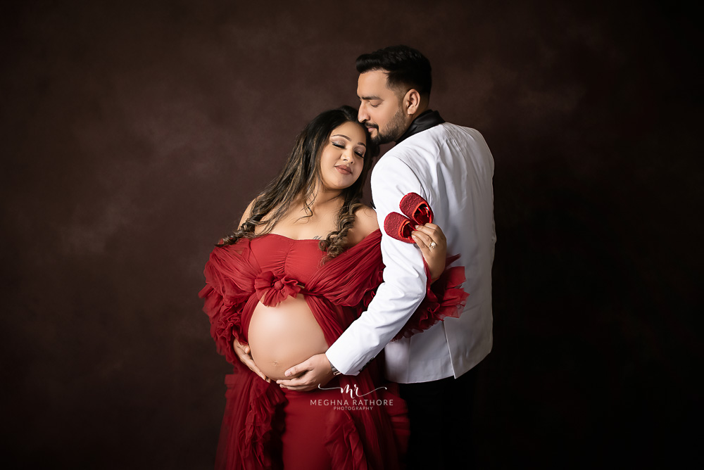Indian couple posing for maternity baby shoot with white plain background.  The couple is posing in a lawn with green grass and the woman is falunting  her baby bump in Lodhi Garden