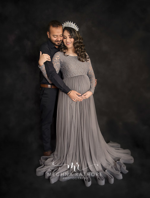 pregnant lady wearing tiara husabnd holding her tummy black backdrop meghna rathore photography