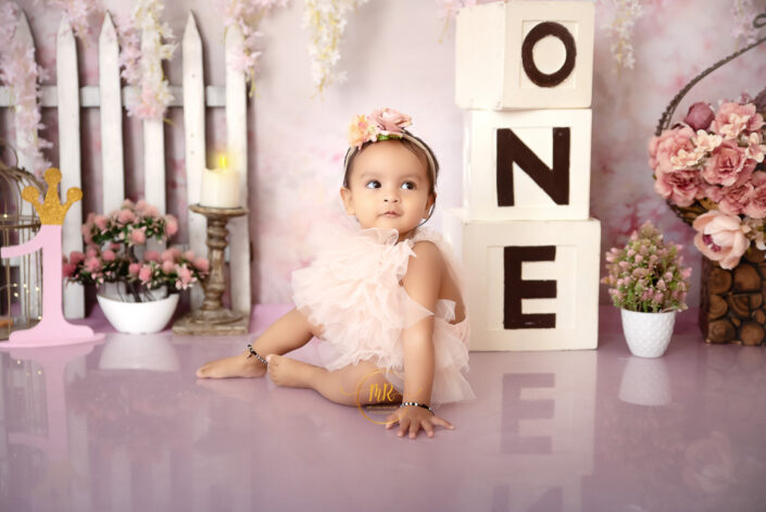 A baby girl in a pink dress playing with three blocks on the floor saying "one" captured by Delhi NCR's best maternal photographer Meghna Rathore.
