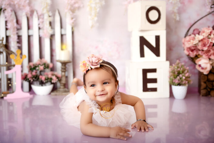A baby girl in a pink dress playing with three blocks on the floor saying "one" captured by Delhi NCR's best maternal photographer Meghna Rathore.