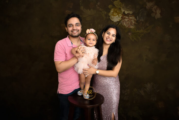 A couple with their newborn posing for a photo in front of a backdrop of flowers captured by Delhi NCR's best maternal photographer Meghna Rathore.