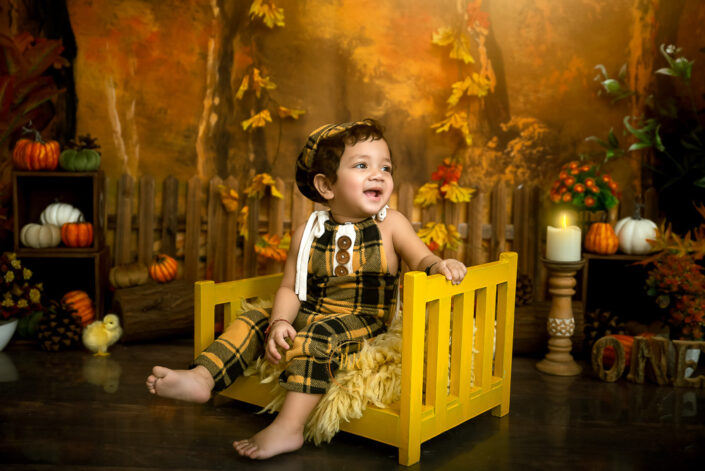 Smiling like a little god a child in a fury wooden bed in an autumn setting Playing with a pumpkin a child in patterned cloths captured by Meghna Rathore Delhi NCR, Haryana best maternity and child photographer.